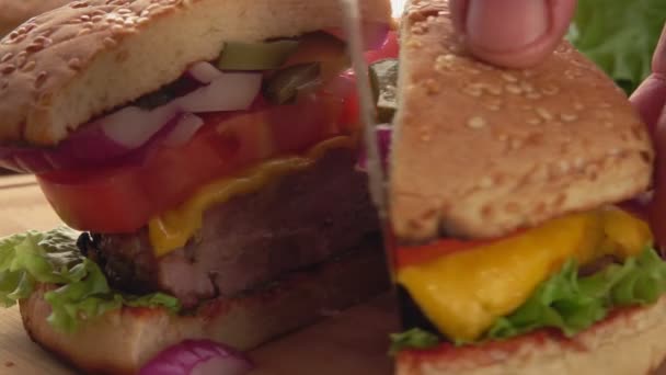 Крупным планом руки разрезают свежий домашний гамбургер пополам ножом — стоковое видео