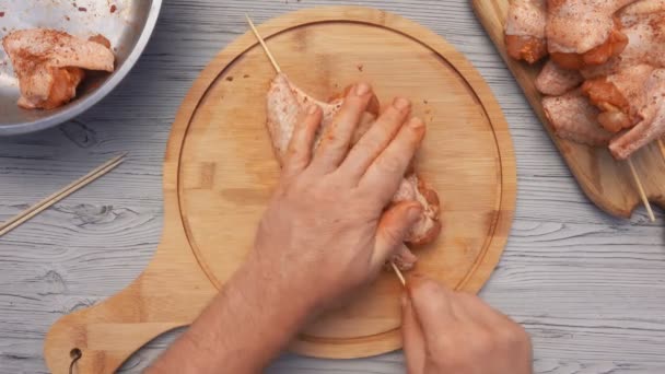 Vista dall'alto delle mani maschili che perforano ali di pollo crude con uno spiedo di legno — Video Stock