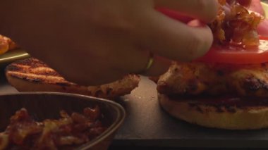 Kadın ellerinin yakın çekiminde tavuk filetosuyla ev yapımı ızgara burger yapıyorlar.