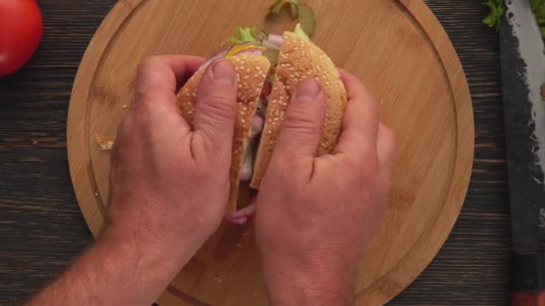 Vista superior de manos masculinas abriendo hamburguesa a la parrilla casera fresca cortada en dos mitades — Vídeo de stock