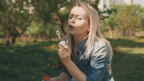 Madre feliz jugando con su hija, soplando burbujas. Mamá de belleza en el parque en slomo — Vídeo de stock