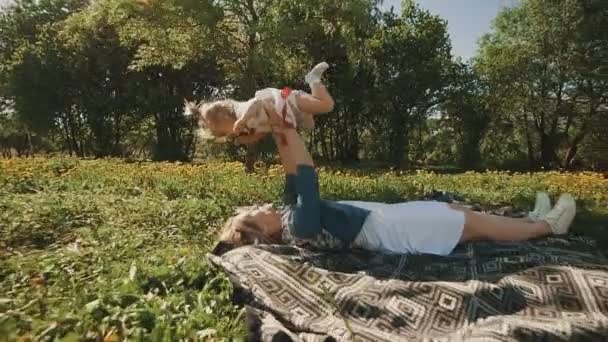 Madre e hija tumbadas en el césped. Familia divirtiéndose en el parque de la ciudad al aire libre — Vídeos de Stock