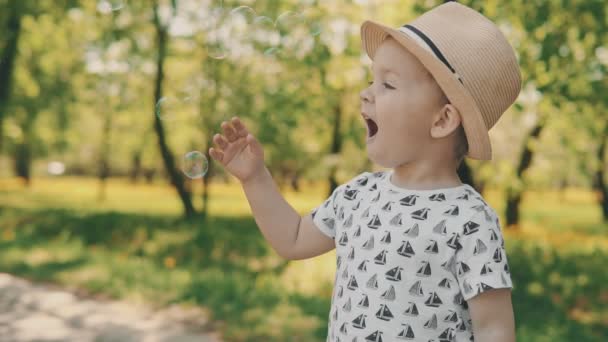 Närbild porträtt av lilla pojken i hat fånga såpbubblor — Stockvideo