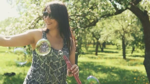 Linda chica divertirse con burbujas de jabón. Joven hermosa mujer juega en el parque — Vídeo de stock