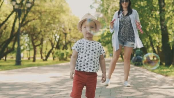 Nahaufnahme Porträt eines kleinen Jungen mit Hut, der Seifenblasen fängt — Stockvideo