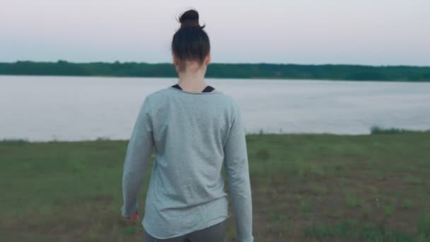 Una joven caminando por la costa por la mañana. Hierba verde, lago. Días de verano — Vídeos de Stock