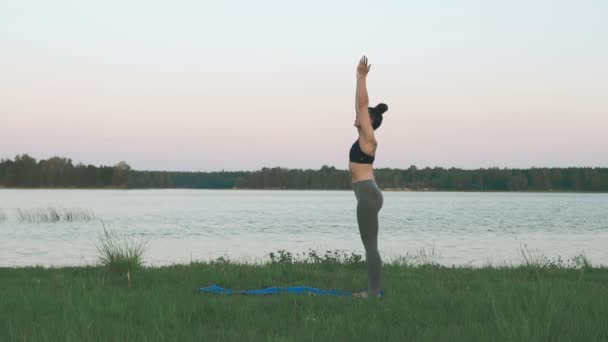 Chica joven con ropa deportiva haciendo yoga en la mañana en el lago con copyspace — Vídeo de stock