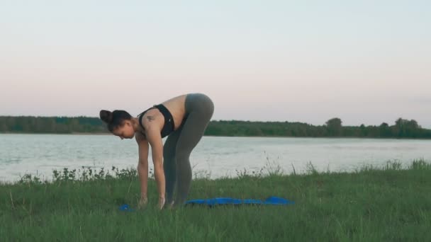 Mujer joven haciendo yoga por la mañana en estera de yoga azul en un paisaje tranquilo — Vídeos de Stock