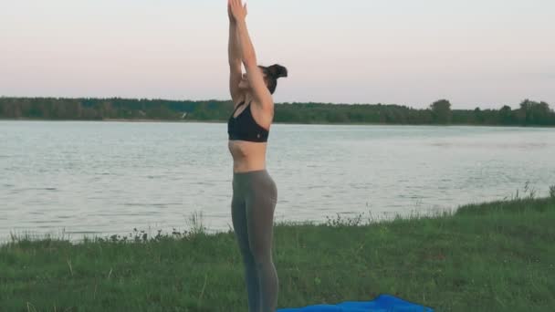 Chica joven en estera de yoga azul en un paisaje tranquilo. Mujer haciendo yoga — Vídeos de Stock