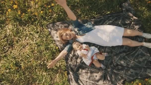 Мать и дочь лежат на лужайке. Счастье материнства и детства — стоковое видео