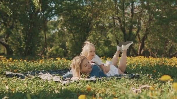 Madre e hija tumbadas en el césped. Felicidad de la maternidad y la infancia — Vídeos de Stock