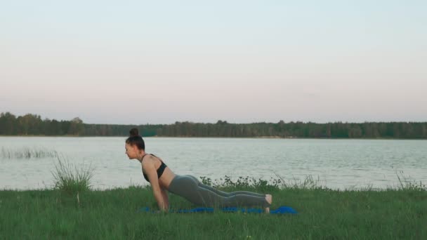 Mujer joven haciendo yoga por la mañana en estera de yoga azul en un paisaje tranquilo — Vídeo de stock