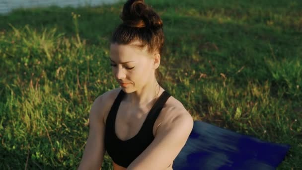 Vrouw doen yoga in ochtend bij lake. Mooi meisje in de lotuspositie bij zonsopgang — Stockvideo