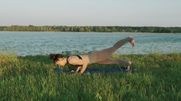 Bruneta žena cvičí jógu v parku. Holka dělá jógu přesune na zelené trávě — Stock video