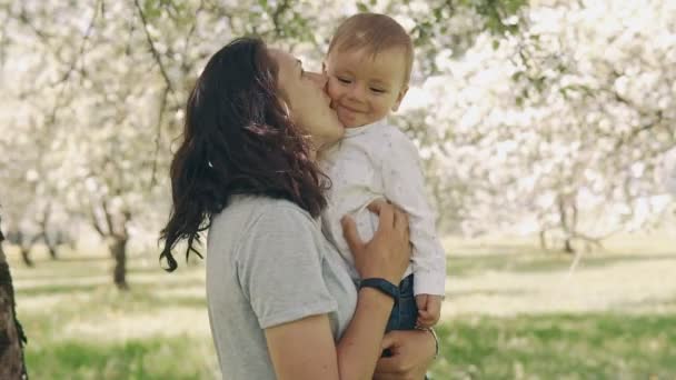 Joven madre y bebé riendo juntos al aire libre. Madre besando pequeño hijo — Vídeos de Stock