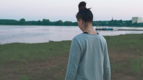 Una joven caminando por la costa por la mañana. Hierba verde, lago. Días de verano — Vídeos de Stock