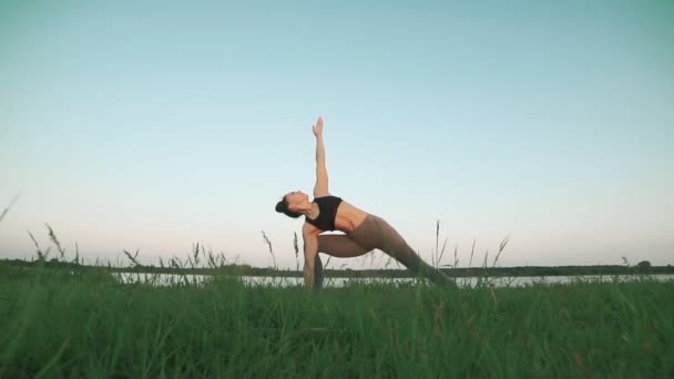 Chica joven en estera de yoga azul en un paisaje tranquilo. Mujer haciendo yoga — Vídeo de stock