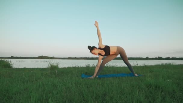 Ung flicka klädd sportkläder gör yoga i morgon vid sjön med copyspace — Stockvideo