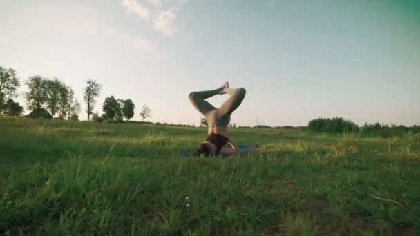 Hermosa mujer practicando yoga por la mañana. Chica haciendo yoga se mueve sobre hierba verde — Vídeo de stock