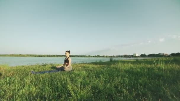 Mooie vrouw in de lotuspositie bij zonsopgang. Meisje doet yoga in ochtend bij lake — Stockvideo