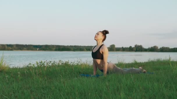 Hermosa joven haciendo yoga por la mañana en estera de yoga azul en un paisaje tranquilo — Vídeos de Stock