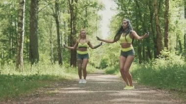 Ağır çekimde Park'ta iki genç kadın atlama ip. Sağlıklı yaşam konsepti. Sarışın ve esmer kızlar açık havada yeşil spor eğitim