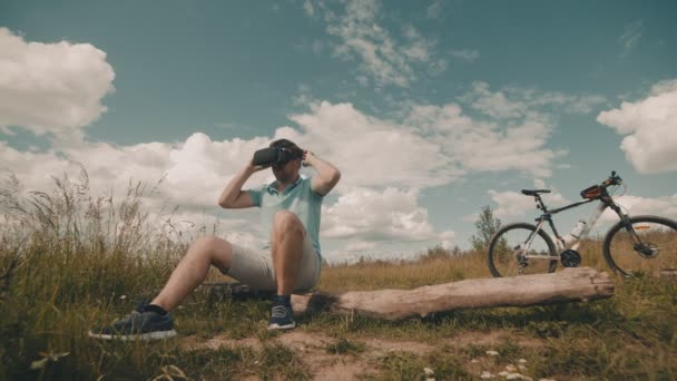 Молодий чоловік використовує VR окуляри на відкритому повітрі, сидячи на дереві — стокове відео