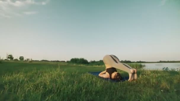Брюнетка практикует йогу в парке. Девушка, занимающаяся йогой, ходит по зеленой траве — стоковое видео