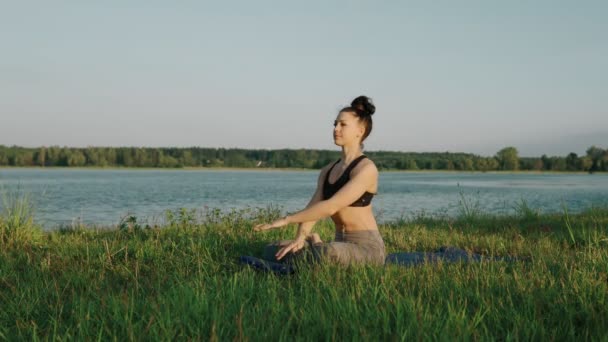 Γυναίκα κάνει γιόγκα το πρωί στη λίμνη. Όμορφο κορίτσι στη θέση lotus στην Ανατολή του ηλίου — Αρχείο Βίντεο