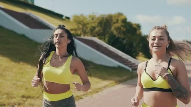 Δύο τρέχοντας γυναικών γυμναστήριο τρέχει στην πόλη στο πρωί. Αθλητική φίλοι τζόκινγκ — Αρχείο Βίντεο