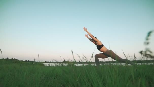 Mujer haciendo yoga. Chica joven en estera de yoga azul en un paisaje tranquilo . — Vídeo de stock