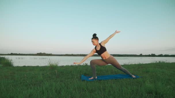 Mujer joven haciendo yoga por la mañana en estera de yoga azul en un paisaje tranquilo — Vídeos de Stock