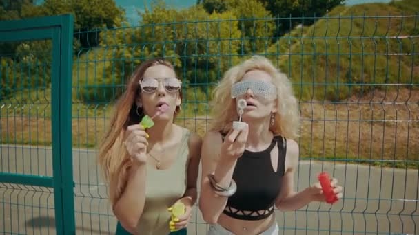 Jolies filles hipster dans des lunettes de soleil s'amuser à faire des bulles à l'extérieur — Video