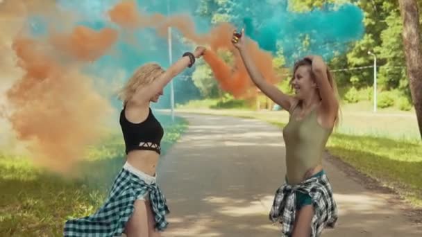 Meninas hipster bonitas em roupas bonitas corre no parque acenando fumaça colorida — Vídeo de Stock