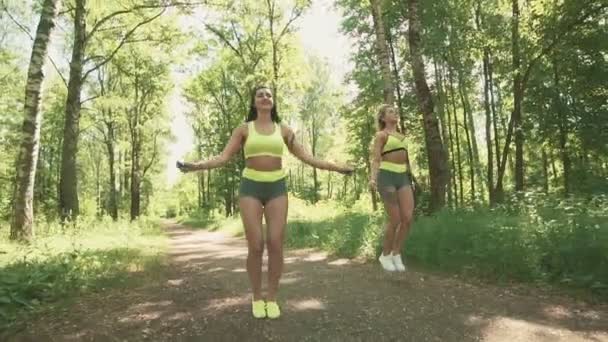 Dos hembras jóvenes saltando la cuerda en el parque en cámara lenta. concepto de estilo de vida saludable — Vídeo de stock