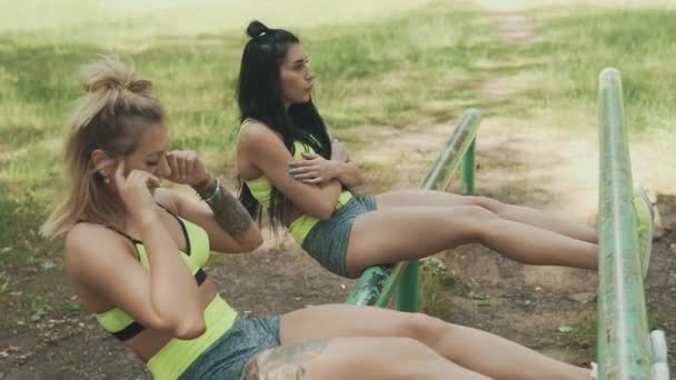 Mujeres jóvenes haciendo ejercicio al aire libre. Chicas rubias y morenas haciendo ejercicios abdominales — Vídeos de Stock