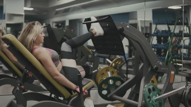 Chica fuerte se dedica a aparatos de entrenamiento deportivo para los músculos de las piernas en el gimnasio — Vídeo de stock