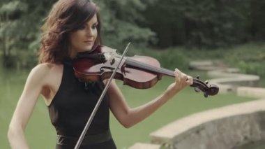 Elbiseli güzel kız açık havada keman çalıyor. Ormandaki zarif kemancı