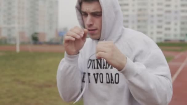 Man in hoodie boxing with invisible opponent at stadium. Young man training — Stock Video