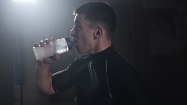 Atleta refrescarse con agua después de un entrenamiento pesado en el gimnasio ahumado oscuro — Vídeos de Stock