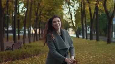 Sevimli kız yaprakları Sonbahar Park savurma ve ağır çekimde gülümseyen ceket