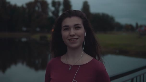 Vrouw ontspannen, luisteren van muziek in het park van de avond. Kijken naar camera — Stockvideo