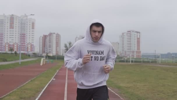 Jovem treinando no estádio de manhã. Boxer correndo com capuz ao ar livre — Vídeo de Stock