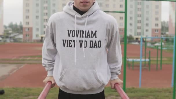 Jonge man in hoodie doen push-ups op parallelle staven stadium in ochtend — Stockvideo