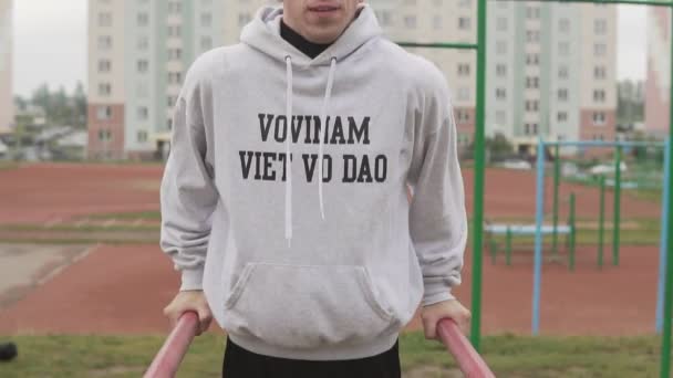 Mladý muž v hoodie dělat kliky na bradla na stadionu v ranní — Stock video