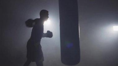 Yalnız boksör sayısı kum torbası yavaş koyu spor salonunda. Kapalı eğitim genç adam. Güçlü atlet spor salonunda. Spor kavram. Orta atış. Dumanlı Studio'da boks sporcu
