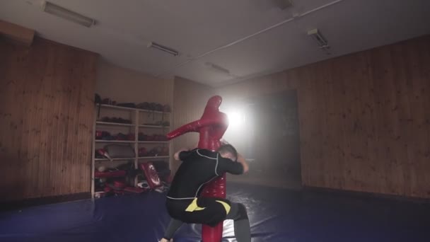 Combatiente golpeando saco de boxeo maniquí en el gimnasio durante la práctica de la técnica de combate — Vídeos de Stock