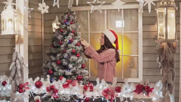 Jong meisje versiert de kerstboom door rode ballen op huis veranda in slomo — Stockvideo