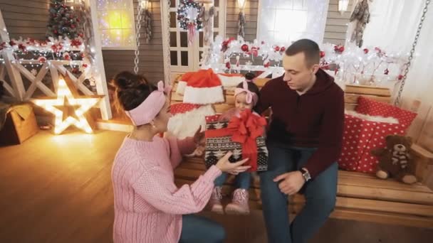 La familia joven da el regalo a la hija en el oscilación de Navidad. Familia sentada en columpio — Vídeo de stock