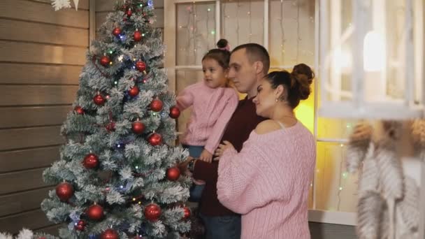 Junge glückliche Familie schmückt gemeinsam Weihnachtsbaum auf Veranda in Zeitlupe — Stockvideo